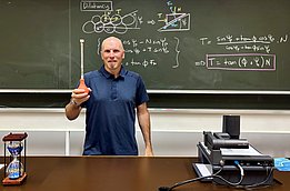 Mann steht vor Tafel mit physikalischen Formeln