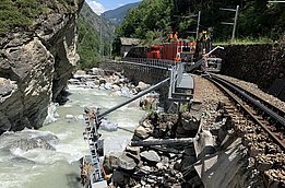 Bauarbeiten an einer beschädigten Eisenbahnstrecke entlang eines Flusses in einem engen Tal mit steilen Felswänden und Wald