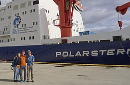 Drei Personen stehen vor dem Forschungsschiff Polarstern am Hafen.