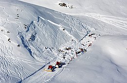 Lawinenabgang an einem schneebedeckten Berghang mit Rettungskräften und Fahrzeugen im Einsatz